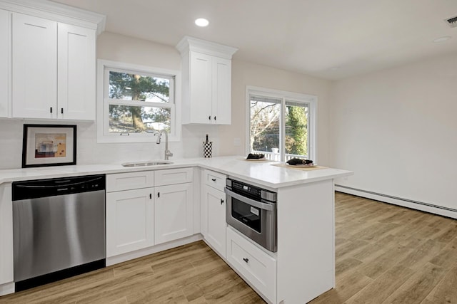 kitchen with appliances with stainless steel finishes, tasteful backsplash, sink, white cabinets, and light hardwood / wood-style floors