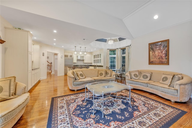 living room with a notable chandelier, vaulted ceiling, and light wood-type flooring