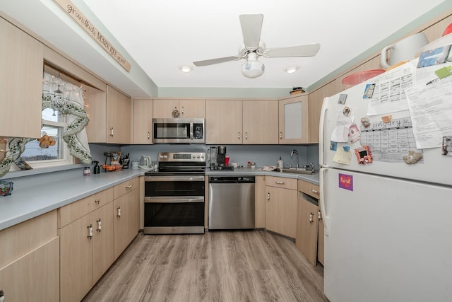 kitchen with stainless steel appliances, ceiling fan, sink, light brown cabinets, and light hardwood / wood-style flooring