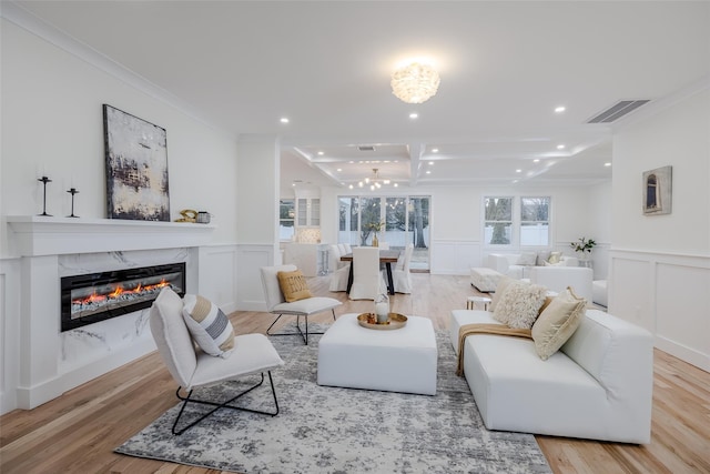 living room featuring a chandelier, ornamental molding, beamed ceiling, a high end fireplace, and light hardwood / wood-style floors