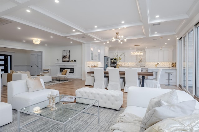 living room with an inviting chandelier, beam ceiling, light hardwood / wood-style flooring, and coffered ceiling