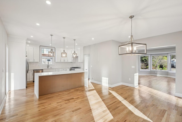 kitchen with a center island, white cabinets, sink, appliances with stainless steel finishes, and decorative light fixtures