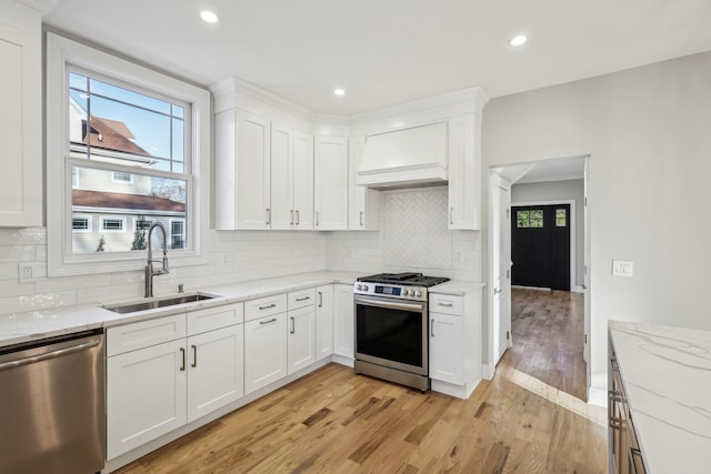 kitchen with white cabinetry, sink, backsplash, custom range hood, and appliances with stainless steel finishes