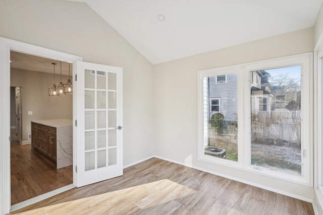 unfurnished room with a notable chandelier, a healthy amount of sunlight, light hardwood / wood-style floors, and vaulted ceiling