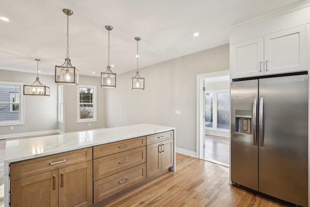 kitchen featuring stainless steel fridge, light stone counters, light hardwood / wood-style flooring, white cabinetry, and hanging light fixtures