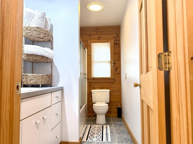 full bathroom with combined bath / shower with glass door, vanity, toilet, and wooden walls