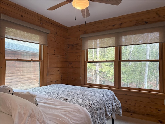 bedroom with ceiling fan, wooden walls, and multiple windows