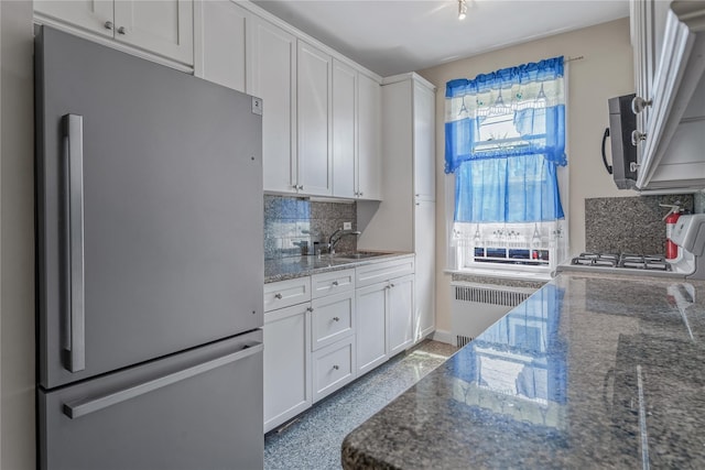 kitchen with decorative backsplash, sink, radiator heating unit, white cabinetry, and stainless steel refrigerator