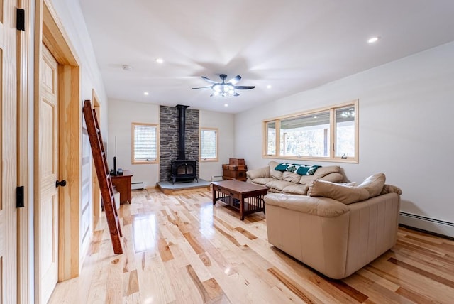 living room with a wood stove, ceiling fan, light hardwood / wood-style flooring, and a baseboard heating unit