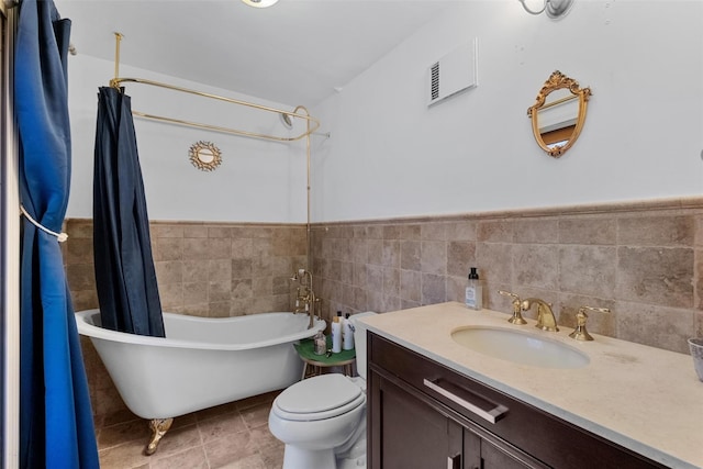 bathroom with toilet, a freestanding tub, tile walls, and wainscoting