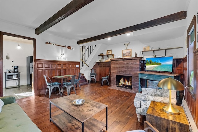 living room with hardwood / wood-style flooring, beam ceiling, and a brick fireplace