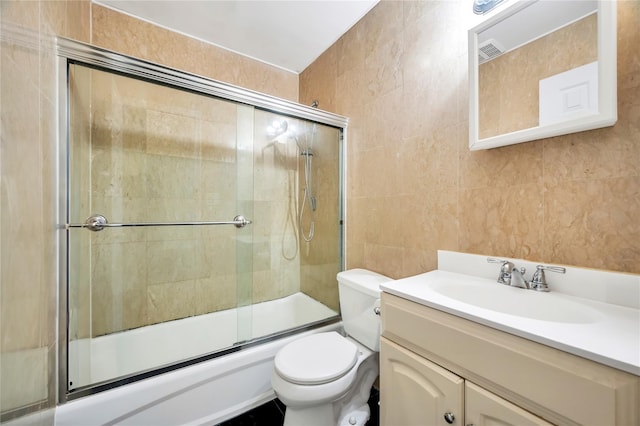 full bathroom with vanity, toilet, combined bath / shower with glass door, and tile walls