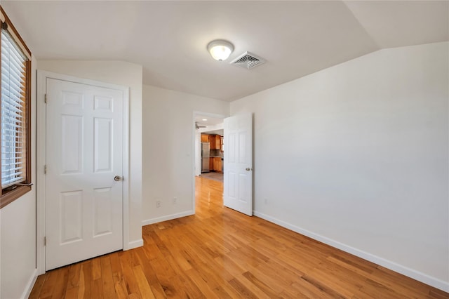 unfurnished bedroom with light wood-type flooring, vaulted ceiling, and stainless steel refrigerator