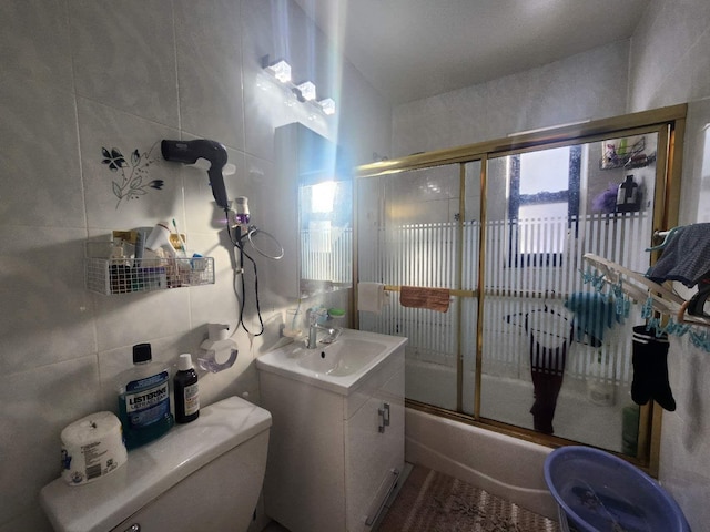 full bathroom with vanity, toilet, bath / shower combo with glass door, and tile walls