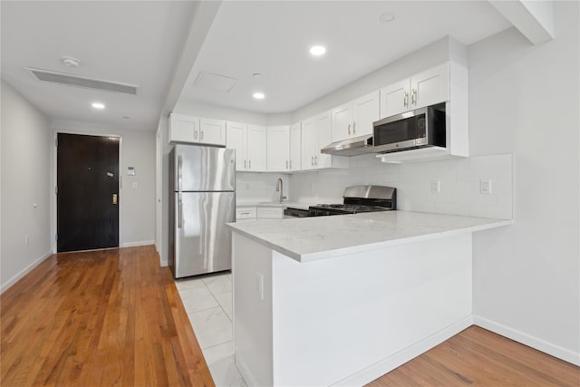 kitchen featuring white cabinets, kitchen peninsula, backsplash, and stainless steel appliances