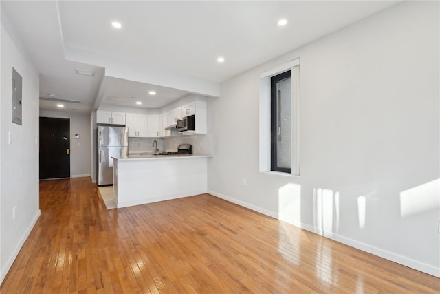 kitchen featuring white cabinetry, kitchen peninsula, stainless steel appliances, backsplash, and electric panel