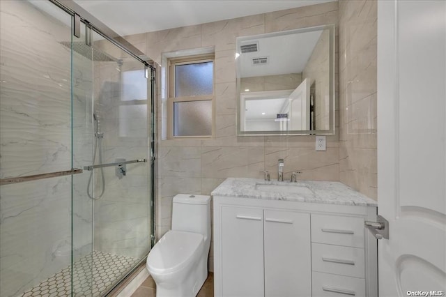 bathroom featuring vanity, toilet, a shower with door, and tile walls