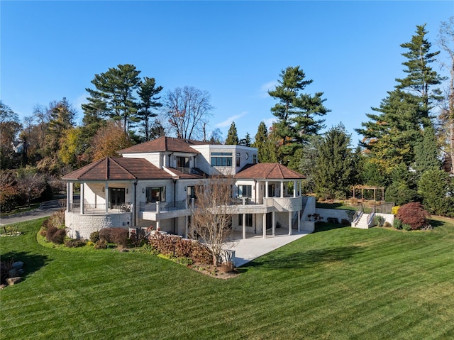 rear view of property with a lawn, a balcony, and a patio