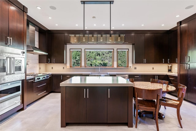 kitchen with dark brown cabinetry, sink, wall chimney exhaust hood, hanging light fixtures, and a kitchen island