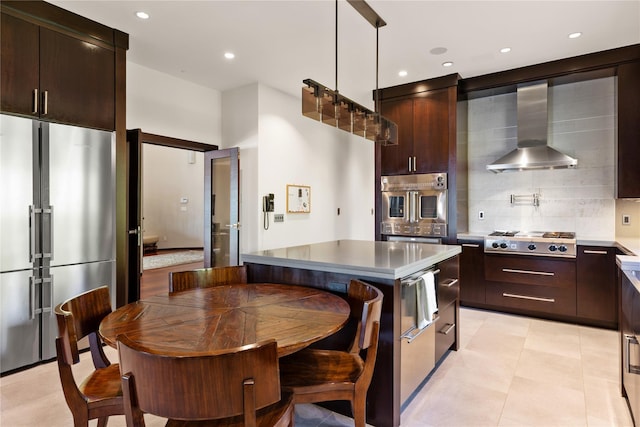 kitchen with a center island, wall chimney exhaust hood, stainless steel appliances, decorative light fixtures, and decorative backsplash