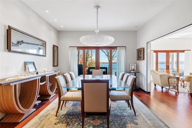 dining area with a wealth of natural light, french doors, a water view, and dark wood-type flooring