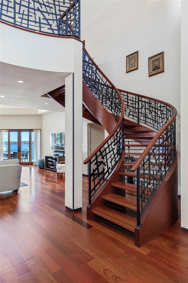 stairway with hardwood / wood-style floors and a towering ceiling