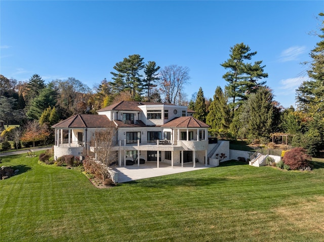 rear view of property featuring a lawn, a balcony, and a patio