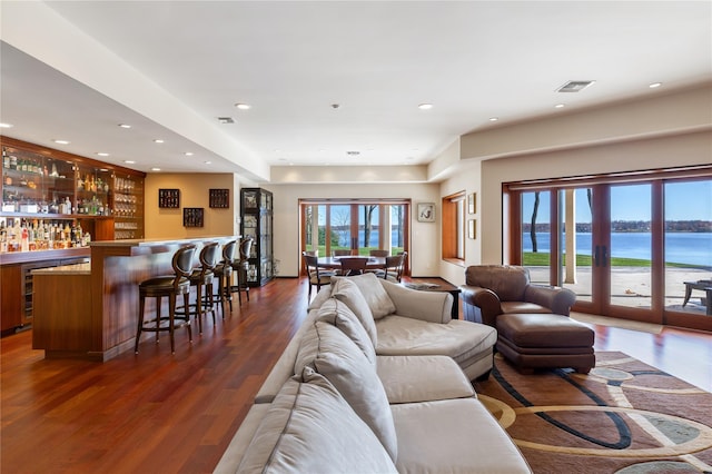 living room with dark hardwood / wood-style flooring, a water view, and bar area