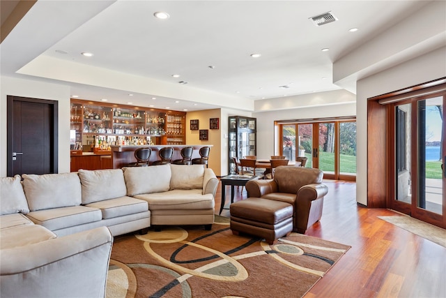 living room with bar area, french doors, and light wood-type flooring