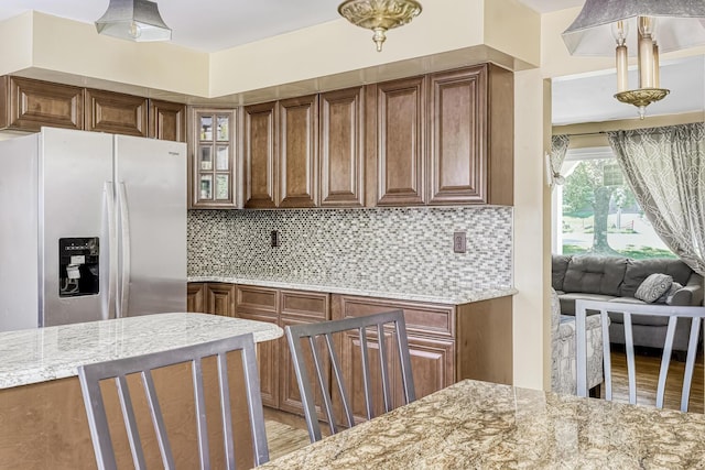 kitchen with tasteful backsplash, stainless steel fridge with ice dispenser, and light stone countertops