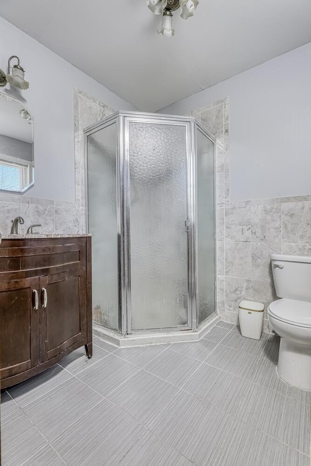 bathroom with tile patterned floors, vanity, tile walls, toilet, and a shower with shower door