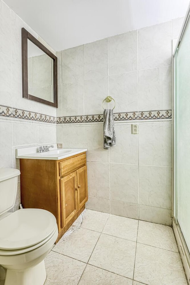 bathroom with vanity, a shower with door, tile patterned floors, toilet, and tile walls