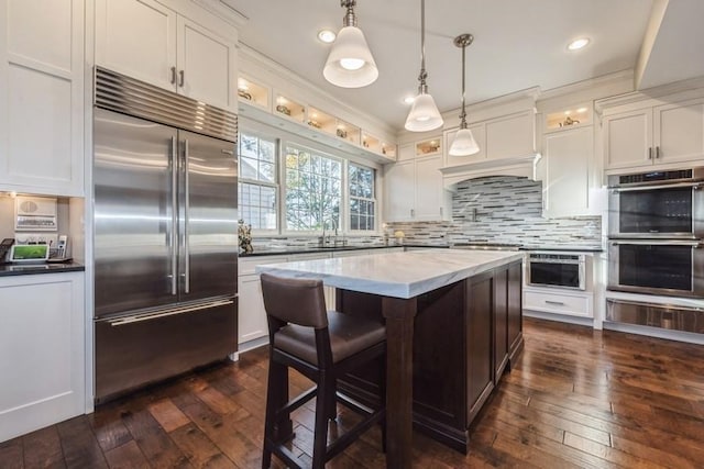 kitchen featuring a kitchen island, decorative light fixtures, tasteful backsplash, white cabinets, and stainless steel appliances