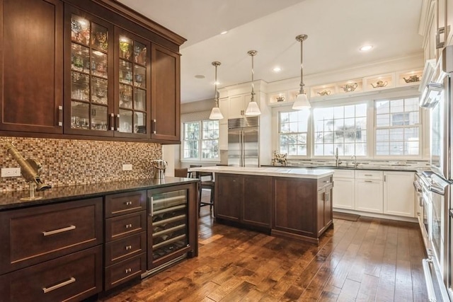 kitchen featuring a kitchen island, decorative light fixtures, stainless steel built in refrigerator, white cabinets, and wine cooler