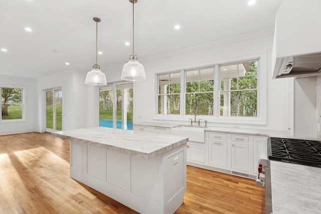 kitchen with pendant lighting, sink, light hardwood / wood-style flooring, white cabinetry, and light stone countertops