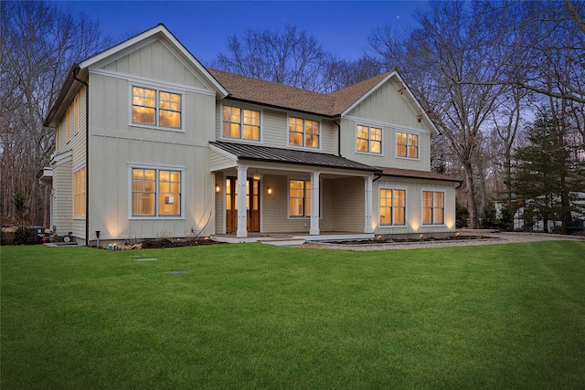 back house at dusk featuring a yard and covered porch