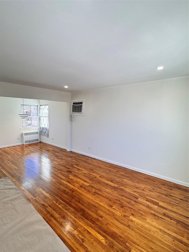 unfurnished room with radiator heating unit, hardwood / wood-style floors, and a wall mounted air conditioner