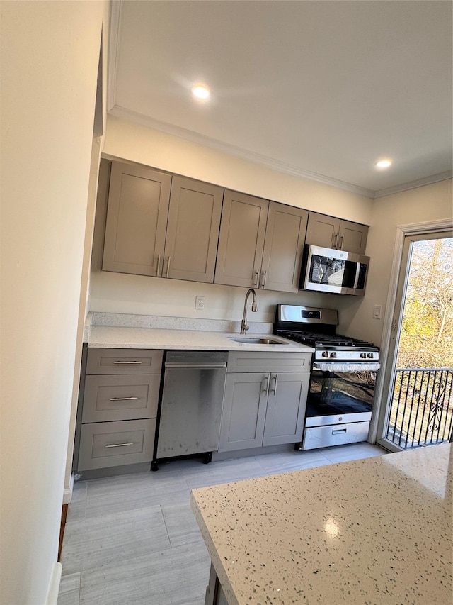 kitchen with appliances with stainless steel finishes, light stone counters, gray cabinetry, crown molding, and sink