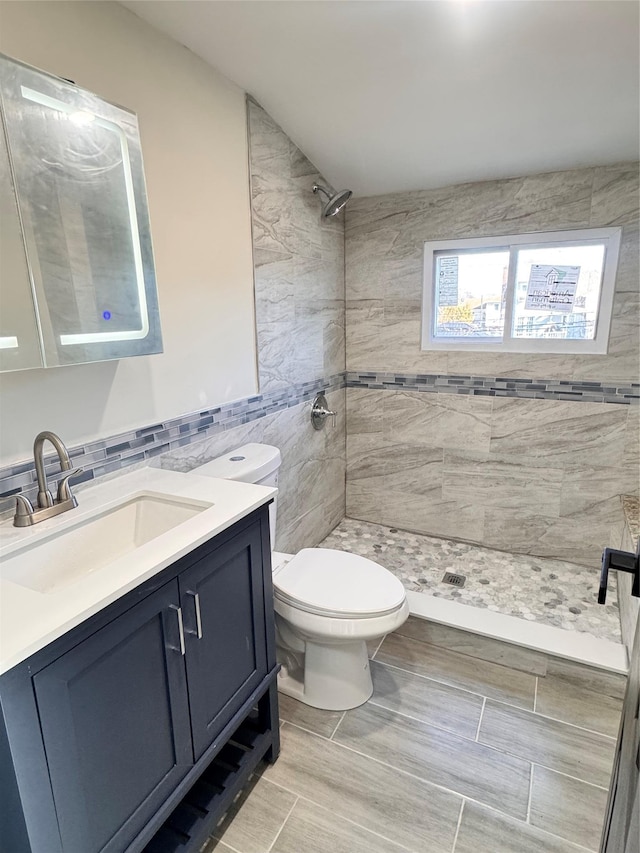 bathroom with tiled shower, vanity, tile walls, and toilet