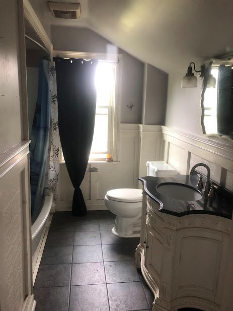 24 Wagner St, Call Listing Agent, NY 13339 - full bath featuring vanity, vaulted ceiling, tile patterned flooring, shower / bath combo with shower curtain, and a wainscoted wall