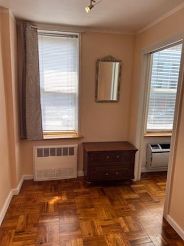 interior space with a wall mounted air conditioner, dark parquet floors, radiator heating unit, and ornamental molding