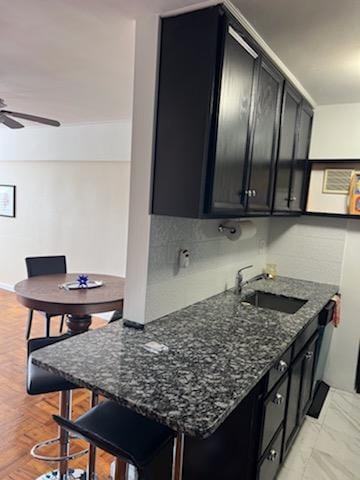 kitchen with a kitchen breakfast bar, ceiling fan, dark stone counters, and sink