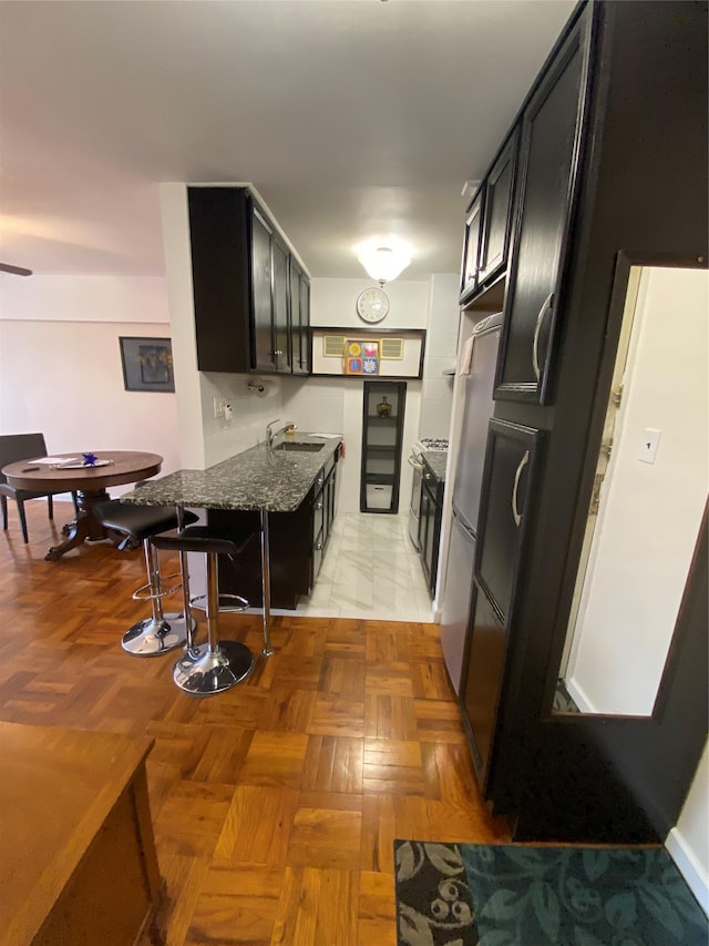 kitchen featuring stainless steel refrigerator, sink, dark stone counters, and light parquet flooring