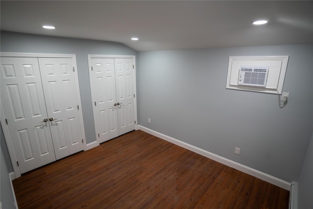 unfurnished bedroom with a wall mounted air conditioner, dark hardwood / wood-style floors, a baseboard radiator, and two closets