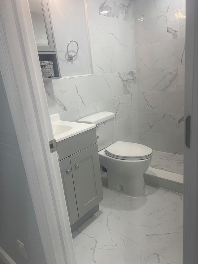 bathroom with vanity, toilet, a shower, and tile walls