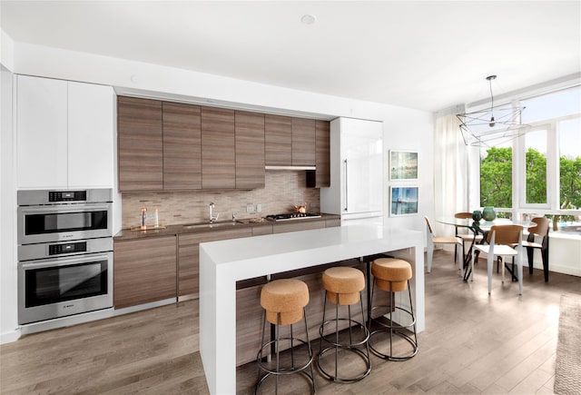 kitchen with white cabinetry, sink, hanging light fixtures, stainless steel appliances, and backsplash