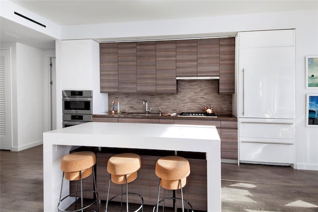 kitchen featuring a breakfast bar, sink, appliances with stainless steel finishes, tasteful backsplash, and dark hardwood / wood-style flooring