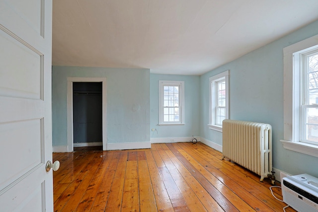 unfurnished room with a wall mounted air conditioner, light hardwood / wood-style floors, and radiator heating unit