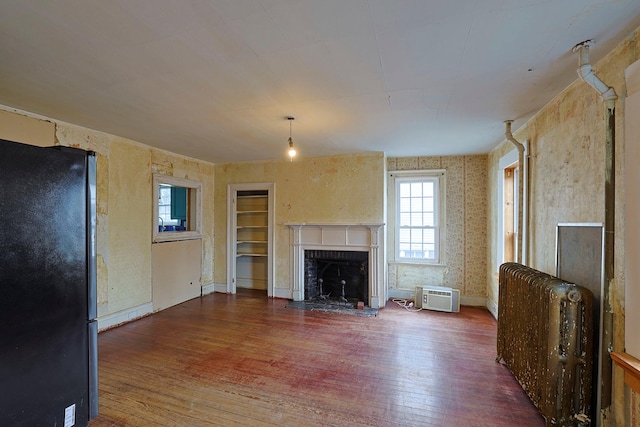 unfurnished living room featuring a brick fireplace, dark wood-type flooring, and a wall unit AC