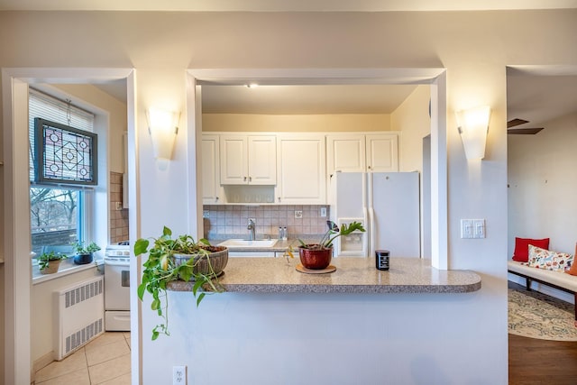 kitchen with tasteful backsplash, white appliances, sink, radiator heating unit, and white cabinetry